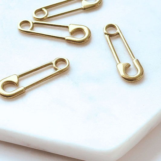 Gold safety pin-shaped charms made from stainless steel with an 18K gold-plated finish, displayed on a white marble surface. Perfect for crafting earrings, necklaces, or bracelets.